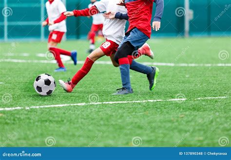 Boys In Red And White Sportswear Plays Soccer On Green Grass Field