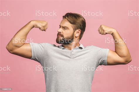 Waistup Portrait Of Muscular Young Man Flexing His Biceps Against Pink