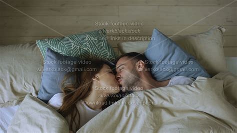 Top View Of Couple Having Fun In Bed Hiding Under Blanket Looking Into Camera And Kissing At