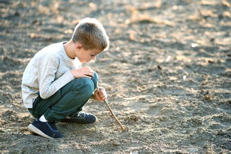 Child Boy Playing With Wooden Stick Digging In Black Dirt Ground