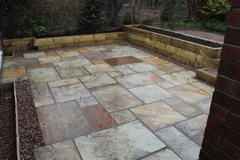 A formal outdoor space with a gravel and long paving stones plus a wooden deck and trees lining the path. Fossil mint Indian stone patio in Sheffield with raised sleeper planters | Patio stones, Garden ...