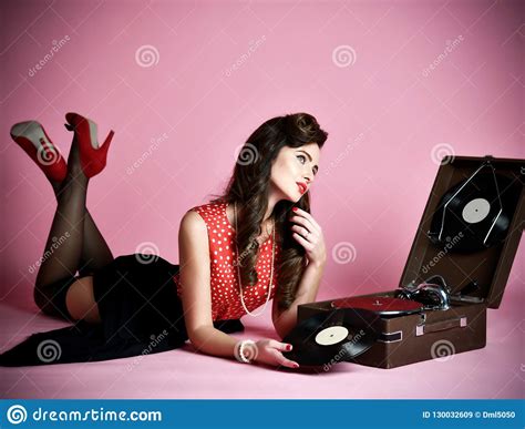 glamorous pinup girl lying near retro gramophone holding lp vinyl record looking up on pink