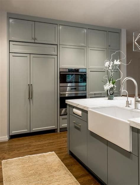View from the side of bottom cupboards and pull down media cabinet with steel fitted cupboard made by empatika london. Gray and white kitchen features a gray rug placed in front ...