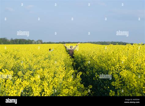 Two Girls Standing In Field Of Canola In Bloom With Arms Raised Mid