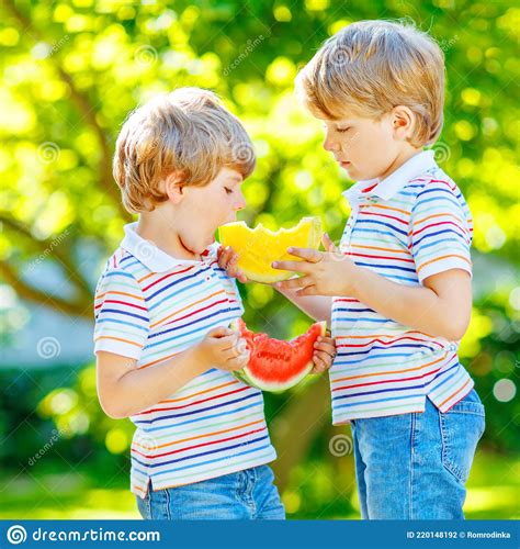 Two Little Preschool Kid Boys With Blond Hairs Eating Red And Yellow