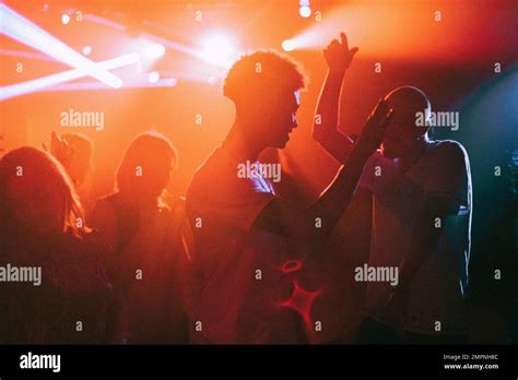 Young men and women dancing against illuminated red spotlights at
