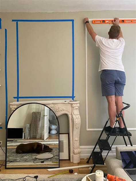 A Man On A Ladder Painting The Wall In His Living Room With Blue Tape