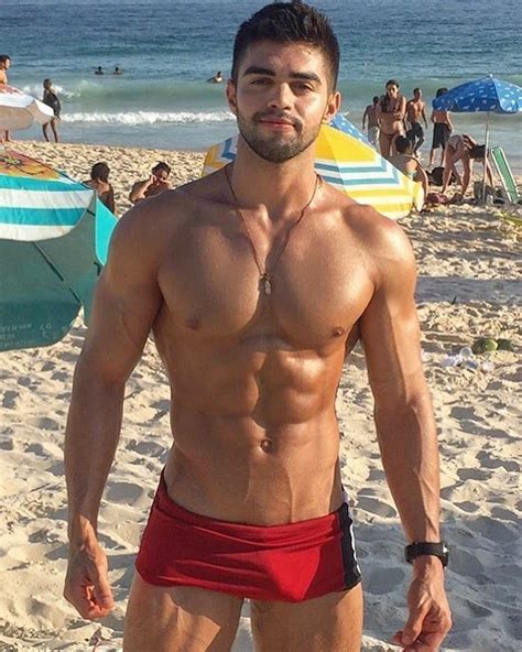A Shirtless Man Standing On The Beach With His Hands In His Pockets And Looking At The Camera