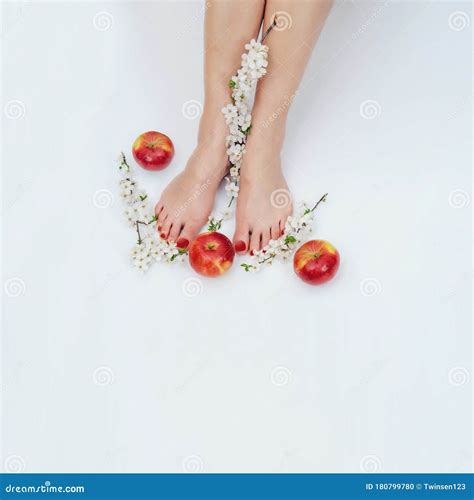 Female Bare Feet On White Background With Apples And Flowers On Cherry Branches On Floor