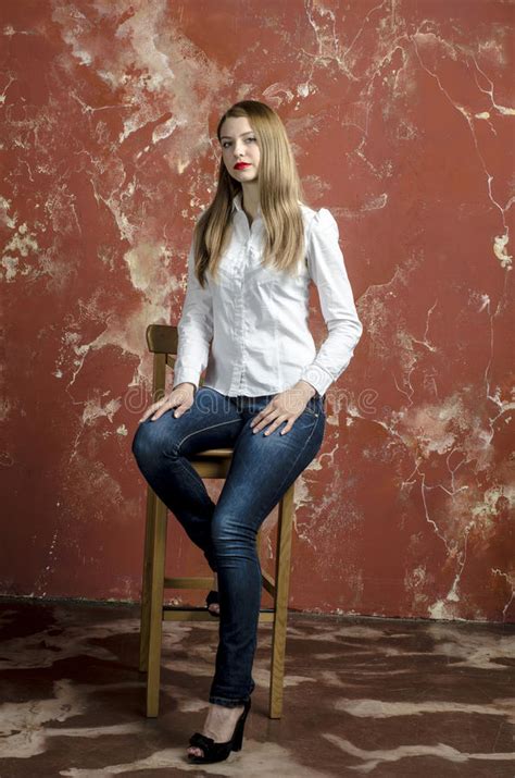 jonge slanke mooie jonge blonde vrouw met lange benen en haar in tumultoverhemd en jeans stock