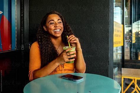 woman smiles holding green juice at cafe by stocksy contributor jayme burrows stocksy