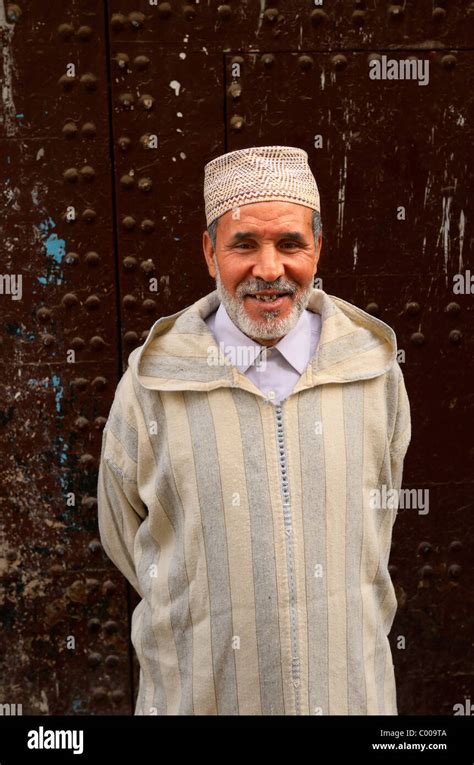 Smiling Moroccan Man In Djellaba And Cap Against An Old Door In El Bali