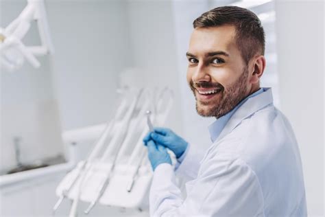 Retrato de un dentista caucásico sonriente sosteniendo un taladro dental y mirando la cámara en