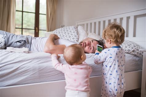 Two toddler children with smartphone and their father on bed in the