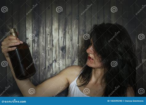 A Young Drunk Woman Looks At The Bottle Of Alcohol With Interest Stock