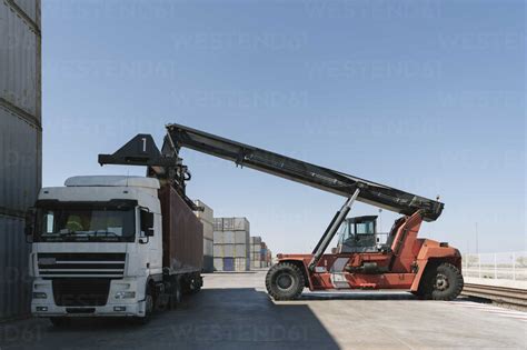 Crane Lifting Cargo Container On Truck On Industrial Site Stock Photo