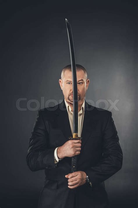 Man In Suit Holding Katana Sword In Front Of His Face On Black Stock