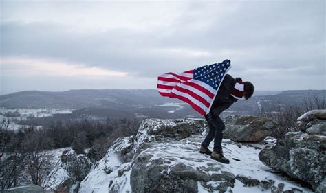 A Climber Holds The American Flag While Standing On The Peak Of A Snowy