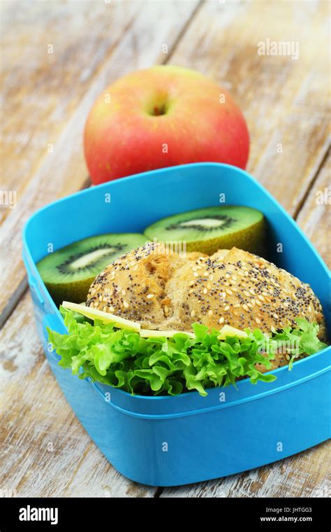 School Lunch Box Containing Wholegrain Cheese Roll With Lettuce Kiwi Fruit And Apple Stock