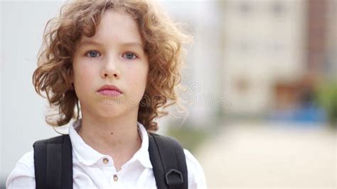 A Close Portrait Of A Serious Blue Eyed Schoolboy With Curly Hair The