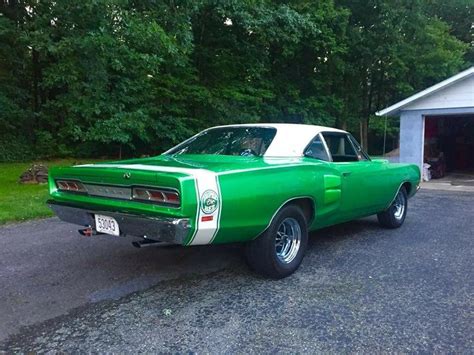 A Green And White Muscle Car Parked In Front Of A Garage With Trees