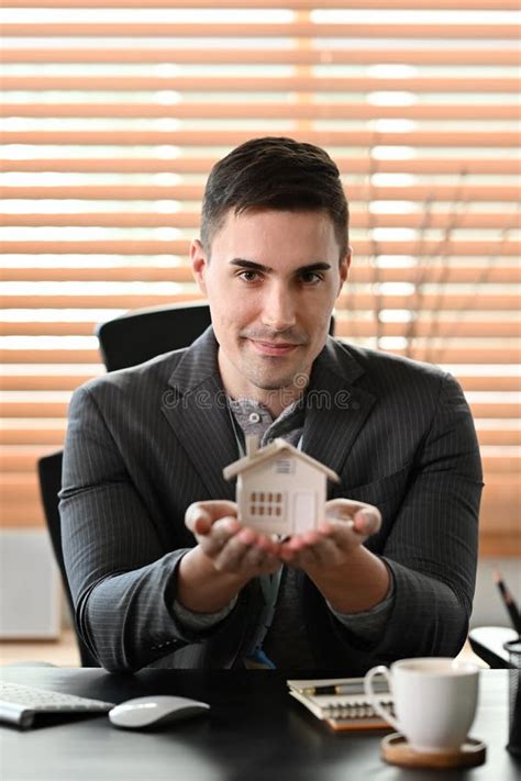 Real Estate Agent Holding Small House Model And Looking At Camera Real