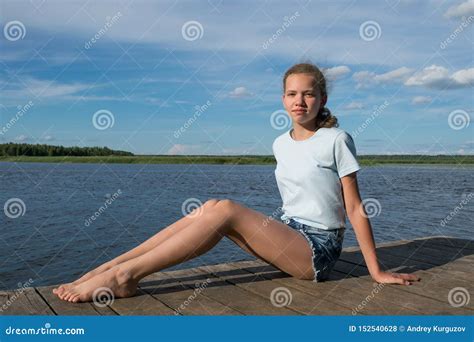 Girl Sitting On A Wooden Pier Against The Blue Cloudy Sky Stock Photo