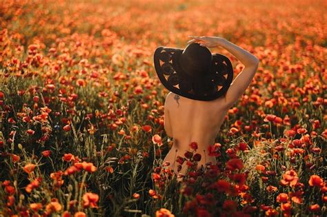 Chica desnuda por detrás con un sombrero negro en un campo de amapolas al atardecer Foto Premium