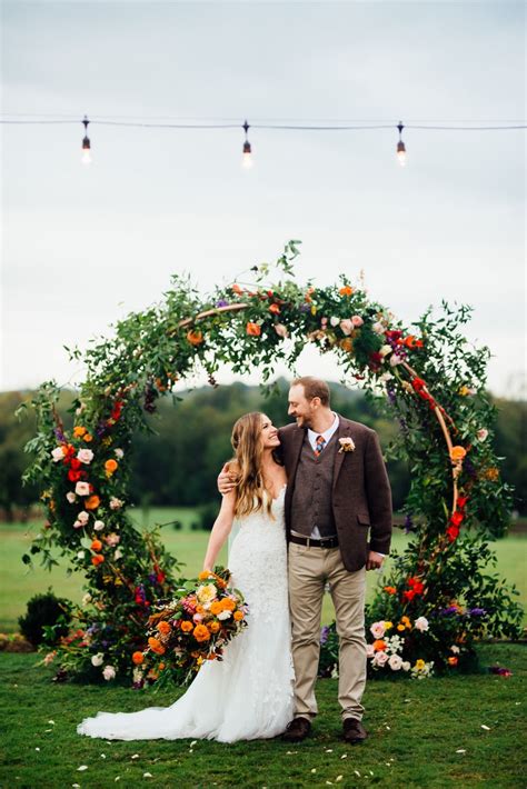 A Bride And Groom Standing In Front Of An Orange Flowered Arch At Their Wedding