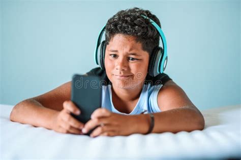 Ethnic Teenage Boy In Headphones Using Smartphone On Bed Stock Image
