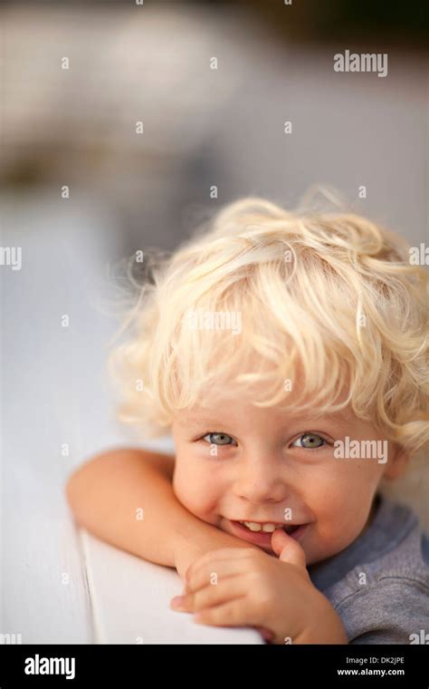Close Up Portrait Of Smiling Blonde Toddle Boy With Curly Hair Leaning