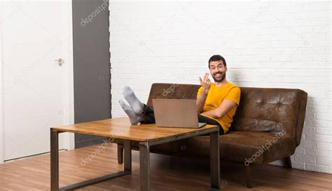 Hombre con su portátil en una habitación invitando a venir con la mano