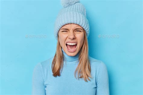 Portrait Of Emotional Angry Woman Screams With Widely Opened Mouth
