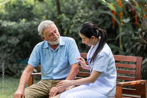 Caring Nurse Helping Senior Man Sitting On Bench In Gaden Asian Woman Caucasian Man Talking