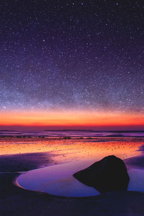 The Night Sky Is Reflected In The Water At The Beach With Stars Above It