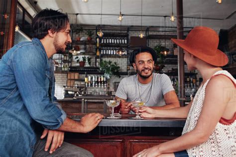 Three Young Friends Smiling And Sitting In A Cafe Having Drinks