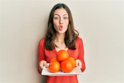 Young Brunette Woman Holding Plate With Fresh Oranges Making Fish Face