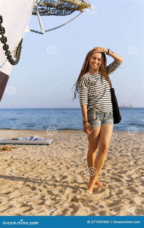 A Girl With A Dreadlocked Hairstyle Poses On The Beach Near A Ship In