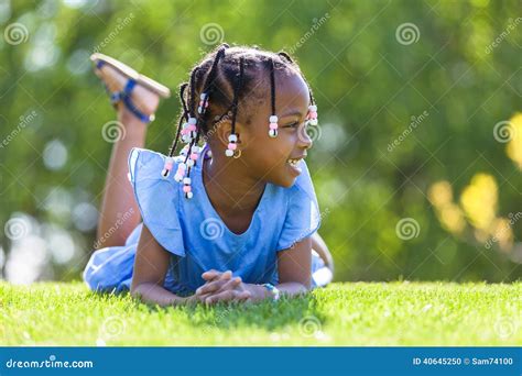 Outdoor Portrait Of A Cute Young Black Girl Lying Down On The G Stock