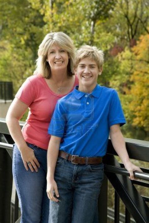 A Blond Mom And Teenage Son Posing Near A Line Of Trees Stock Photo