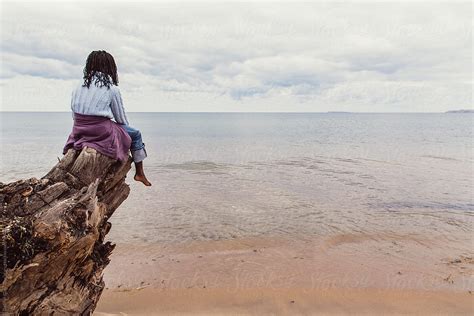 african american girl sitting on a tree log looking over the sea by stocksy contributor gabi