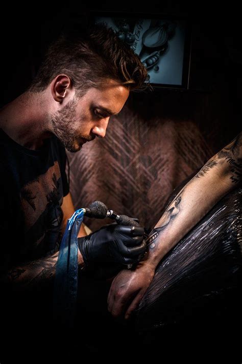 A Man With Tattoos On His Arm Getting Inked By Another Man In The Dark