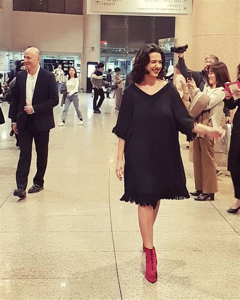 A Woman In A Black Dress And Red Boots Walking Through An Airport With