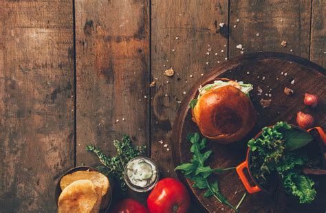 Burger And Vegetables Placed On Brown Wood Surface · Free Stock Photo