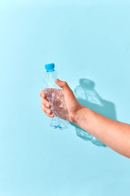 Premium Photo Empty Plastic Bottle Crushed By Hand On A Pastel Blue Wall With Transparent