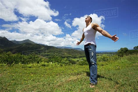 A Young Man Standing In A Grass Field With Arms Outstretched Looking Up