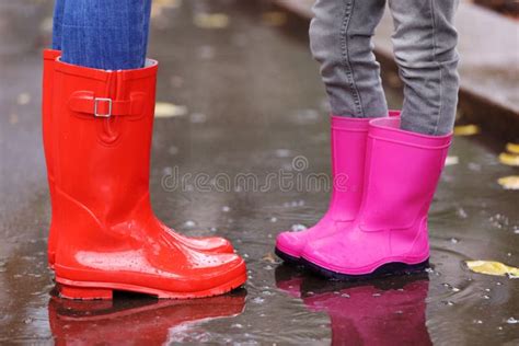 Mother And Daughter Wearing Rubber Boots Standing In Puddle On Rainy