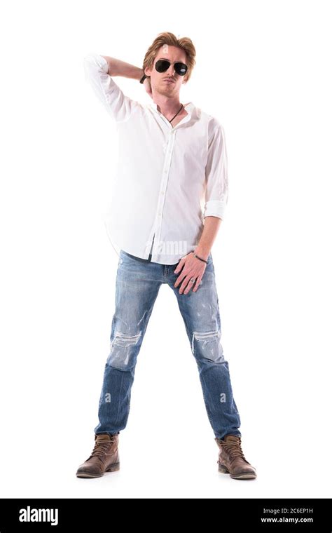 Guapo estilo hombre modelo de moda en jeans rasgados camisa blanca posando con la mano detrás de