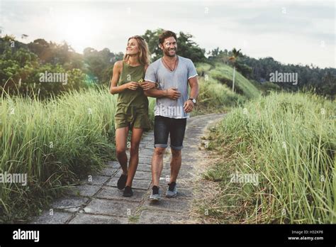 Outdoor Shot Of Young Couple In Love Walking On Pathway Through Grass Field Man And Woman