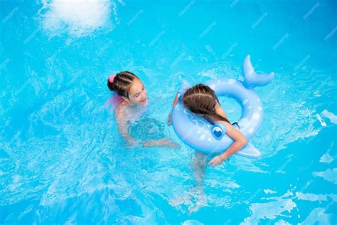 Две девочки сестры плавают в бассейне с голубой водой и устраивают фан